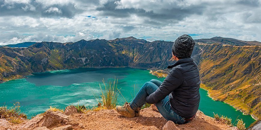 Kvinna sitter på kanten av kratersjön Quilotoa i Ecuador.