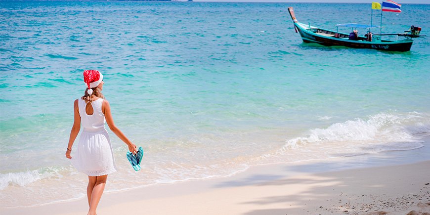 Kvinna promenerar på stranden i Thailand iklädd tomteluva