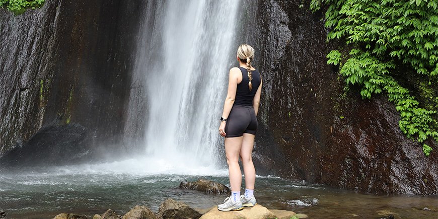 Louisa står framför vattenfallet Red Coral Waterfall